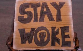 Man holding a cardboard sign that says "Stay Woke"